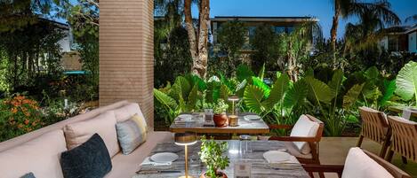 Un comedor al aire libre con una mesa de madera dispuesta para dos personas, rodeado de exuberante vegetación y palmeras.