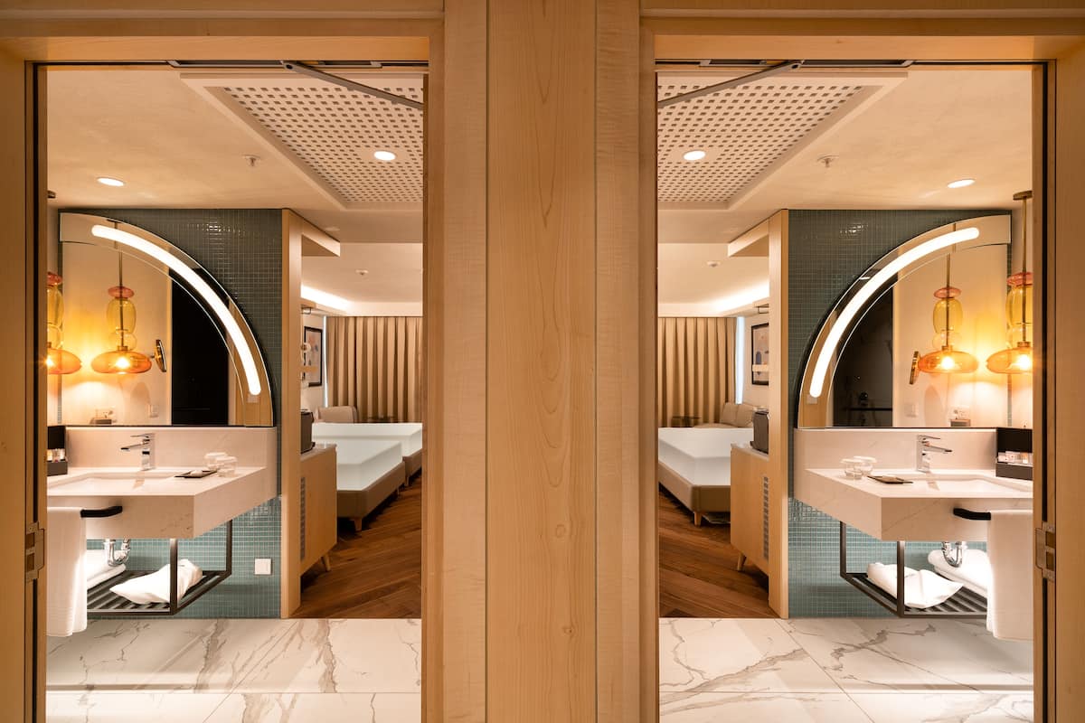 A mirrored view of a modern bathroom with a marble floor, a wooden vanity, and a curved mirror.