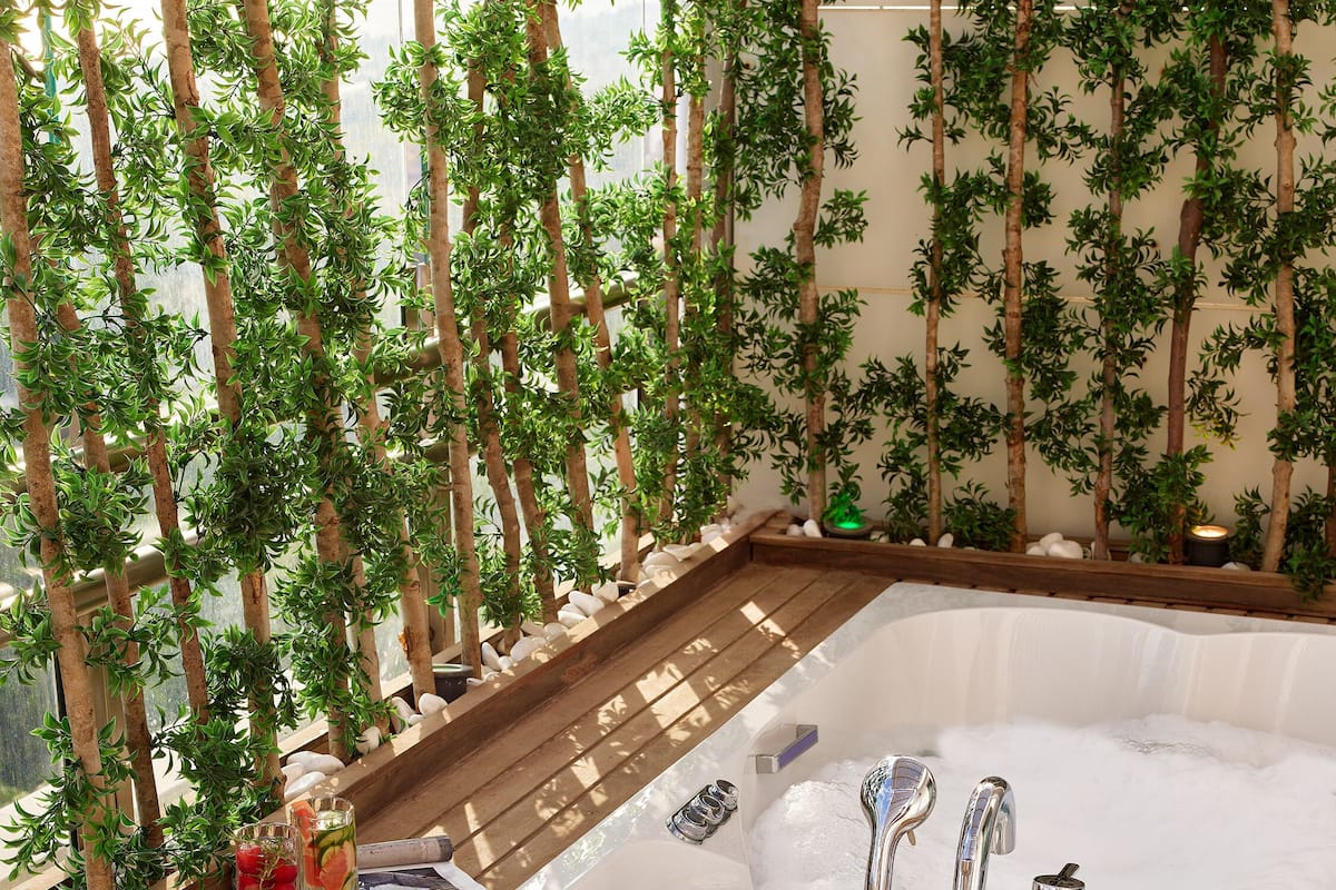 A hot tub with wooden steps and a wooden deck, surrounded by artificial greenery.