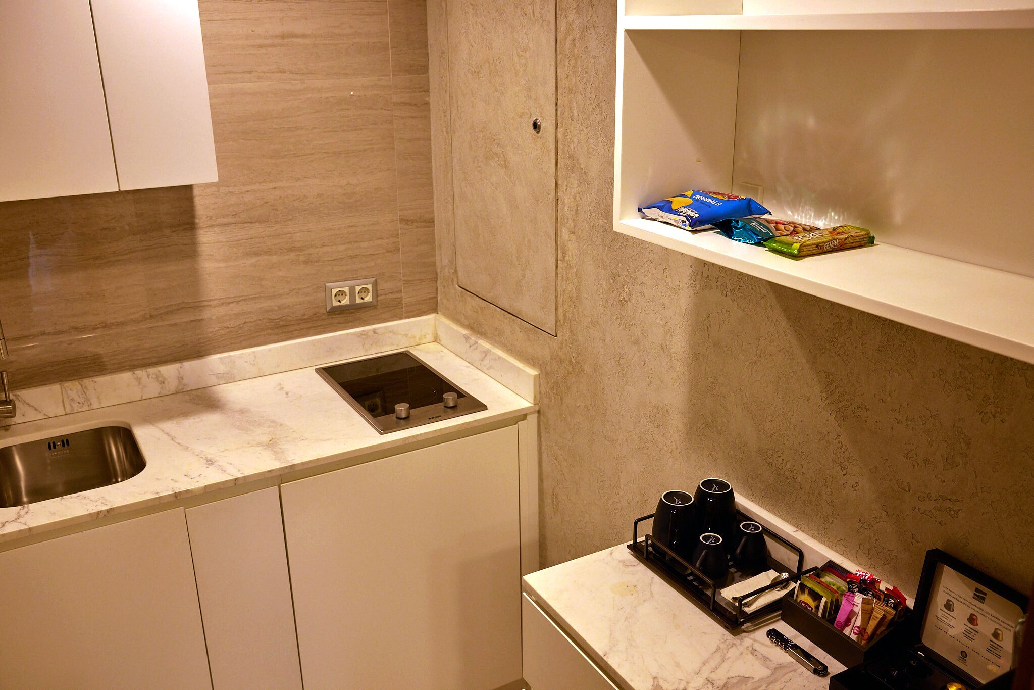 A kitchen with a sink, a built-in stove, and a countertop with a coffee maker and a box of snacks.