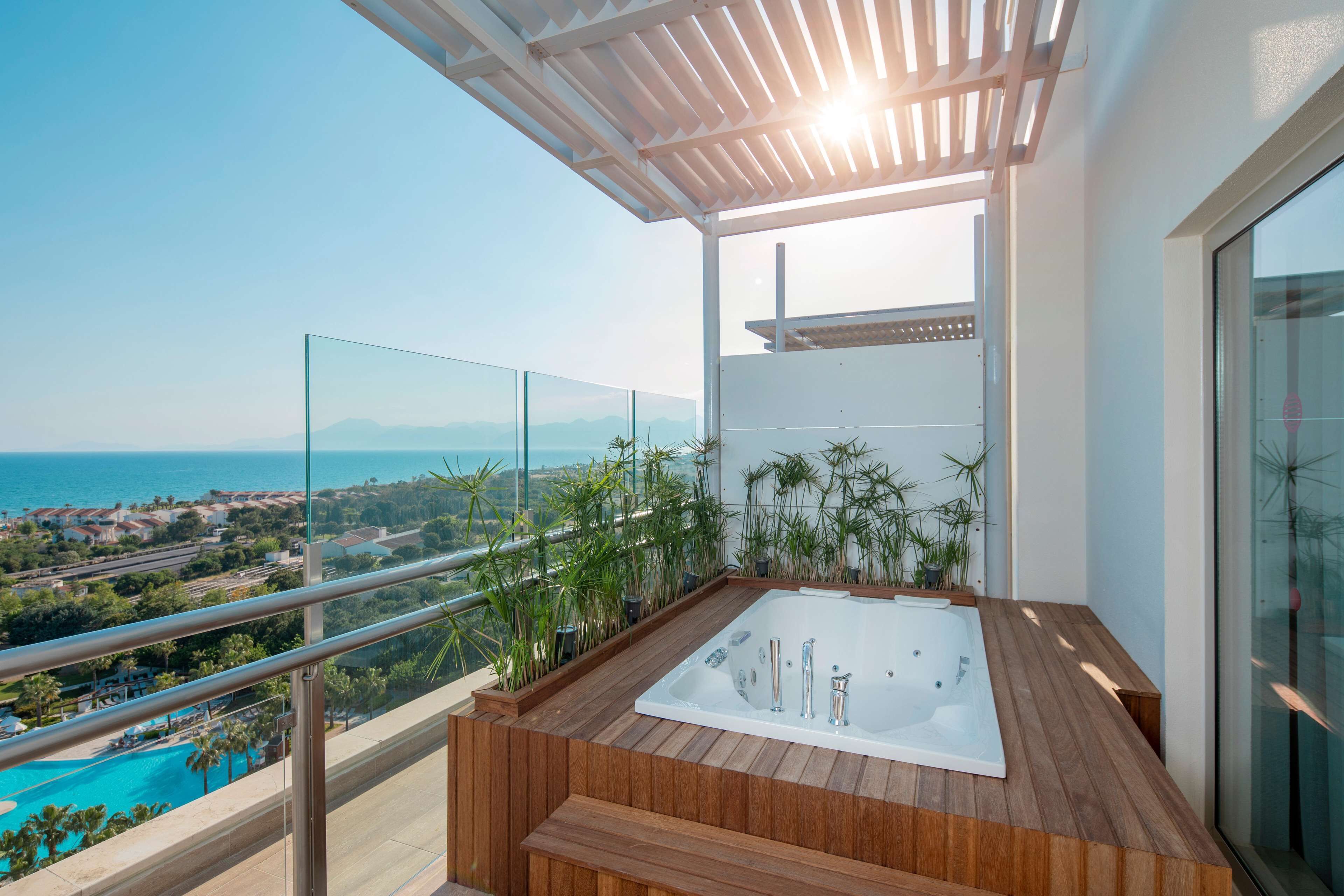 A balcony with a wooden hot tub, glass railings, and a view of the sea.