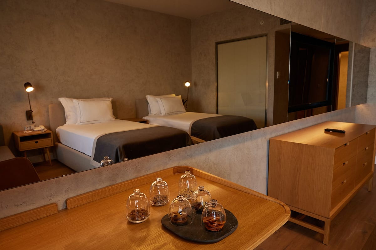 A hotel room with two beds, a wooden desk with a tray of snacks, and a minibar.
