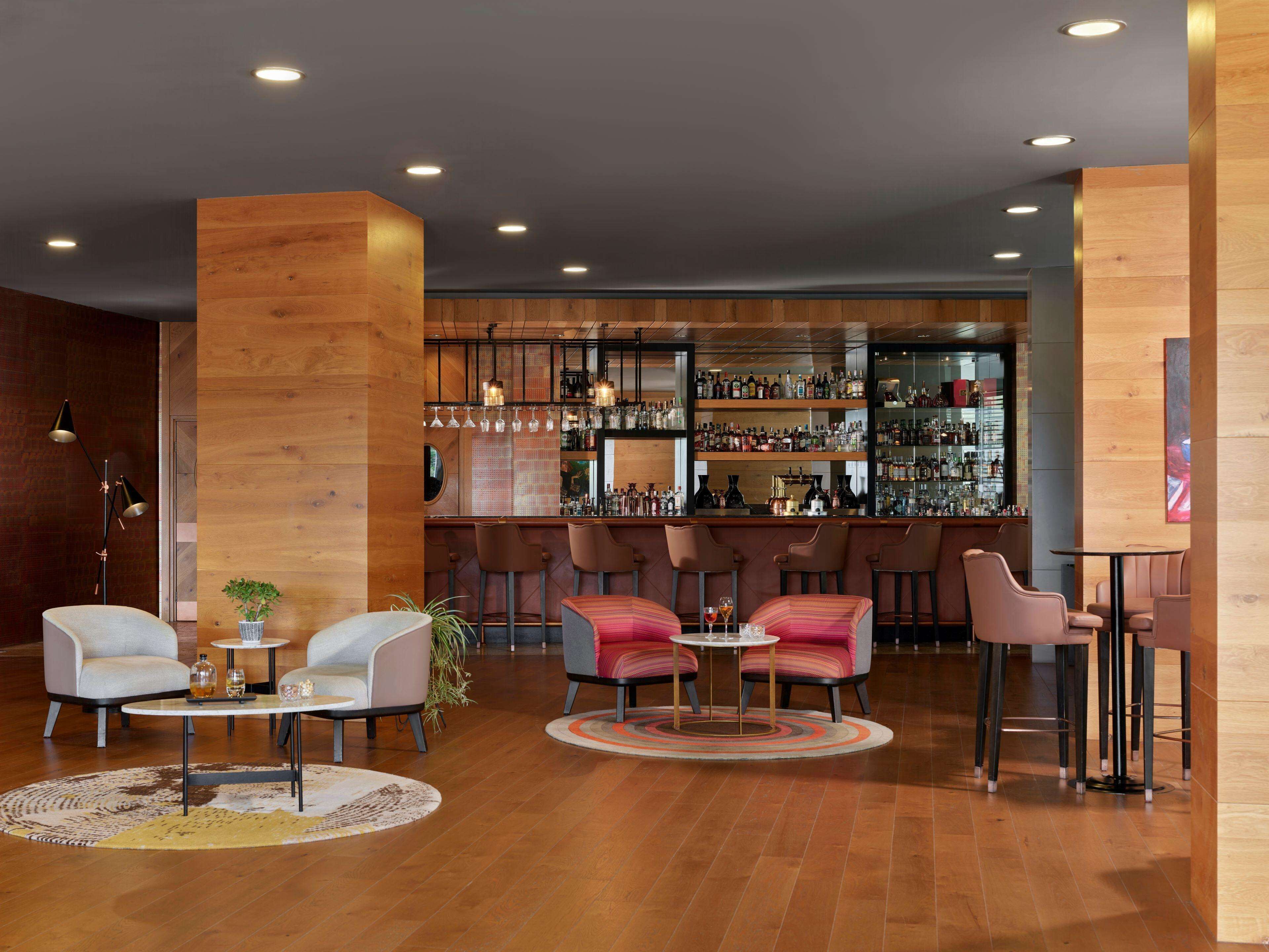 A modern bar area with wooden accents, bar stools, and a variety of bottles on shelves.