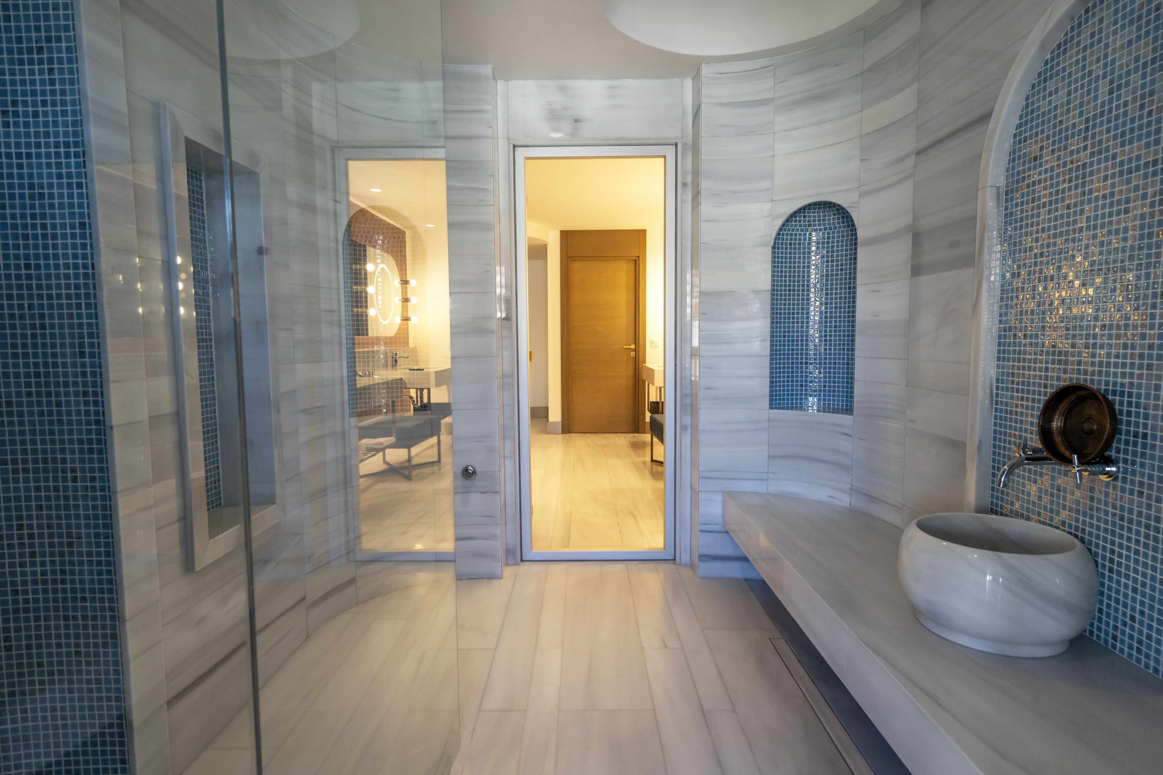 A modern bathroom with a marble floor, a large sink, and a glass shower enclosure.