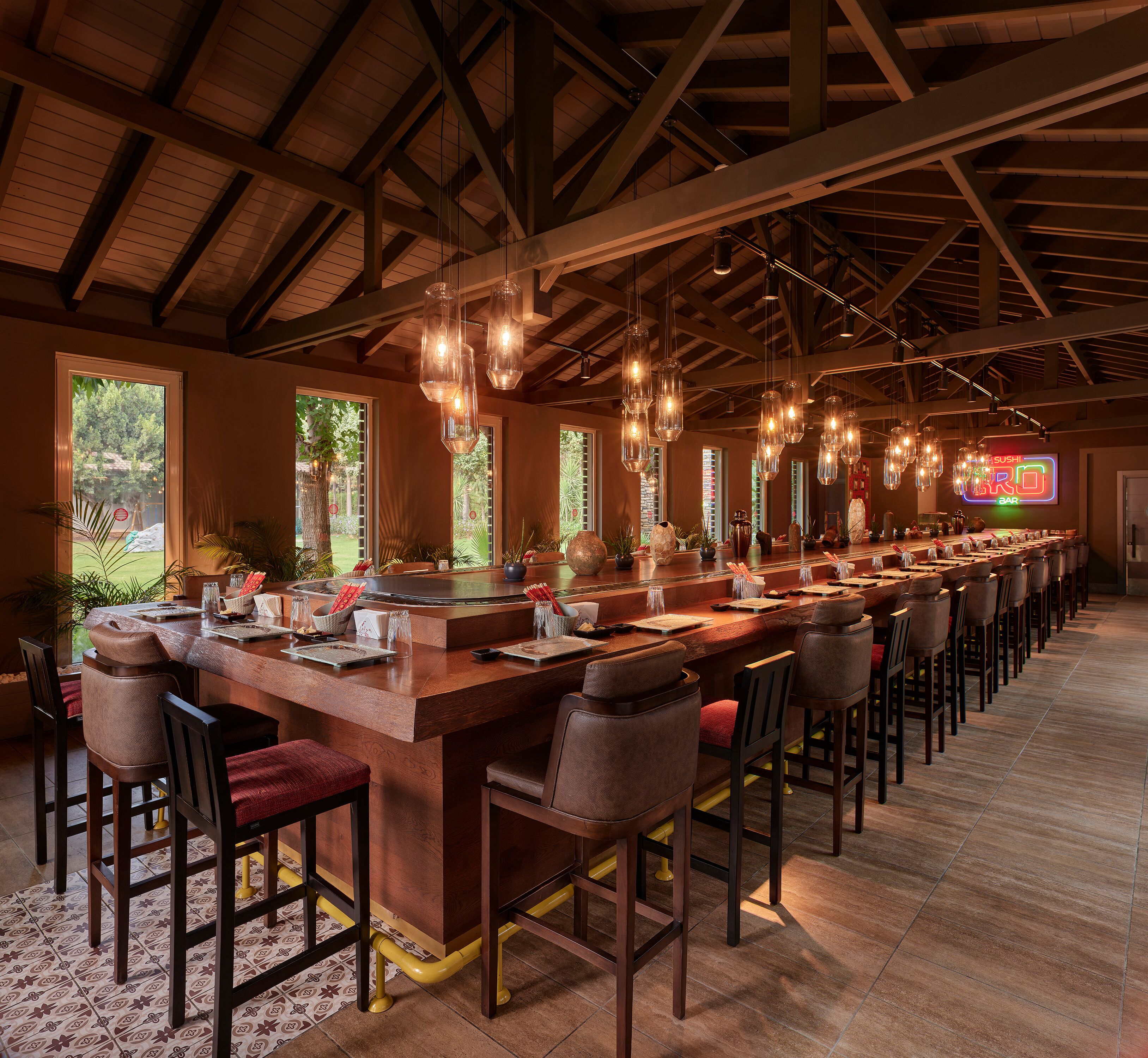 A long bar area with multiple stools and hanging pendant lights.