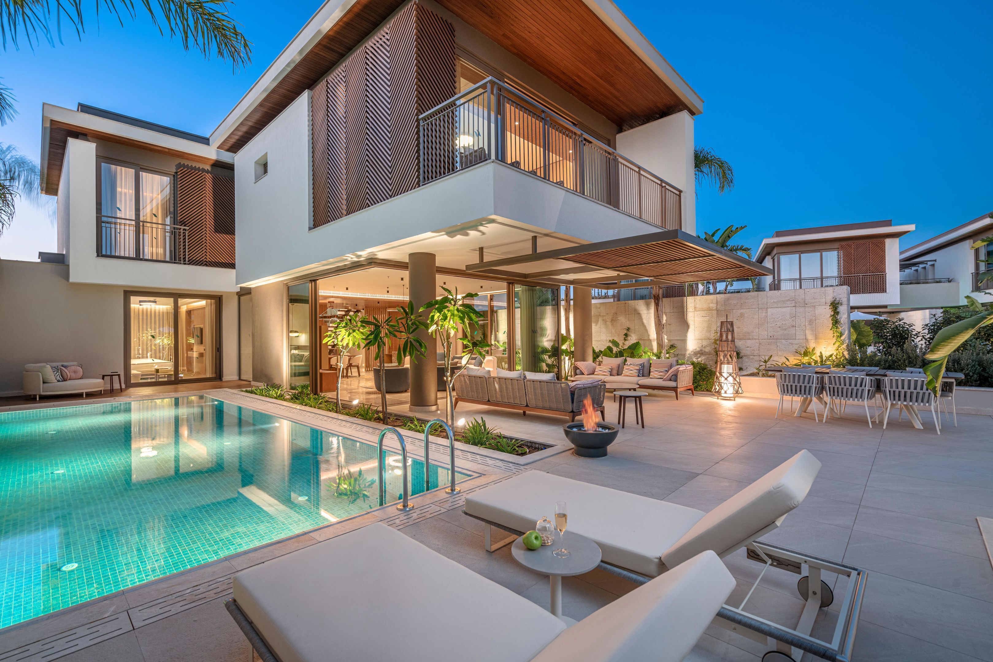 A modern two-story house with a swimming pool, outdoor seating, and a well-lit patio area.