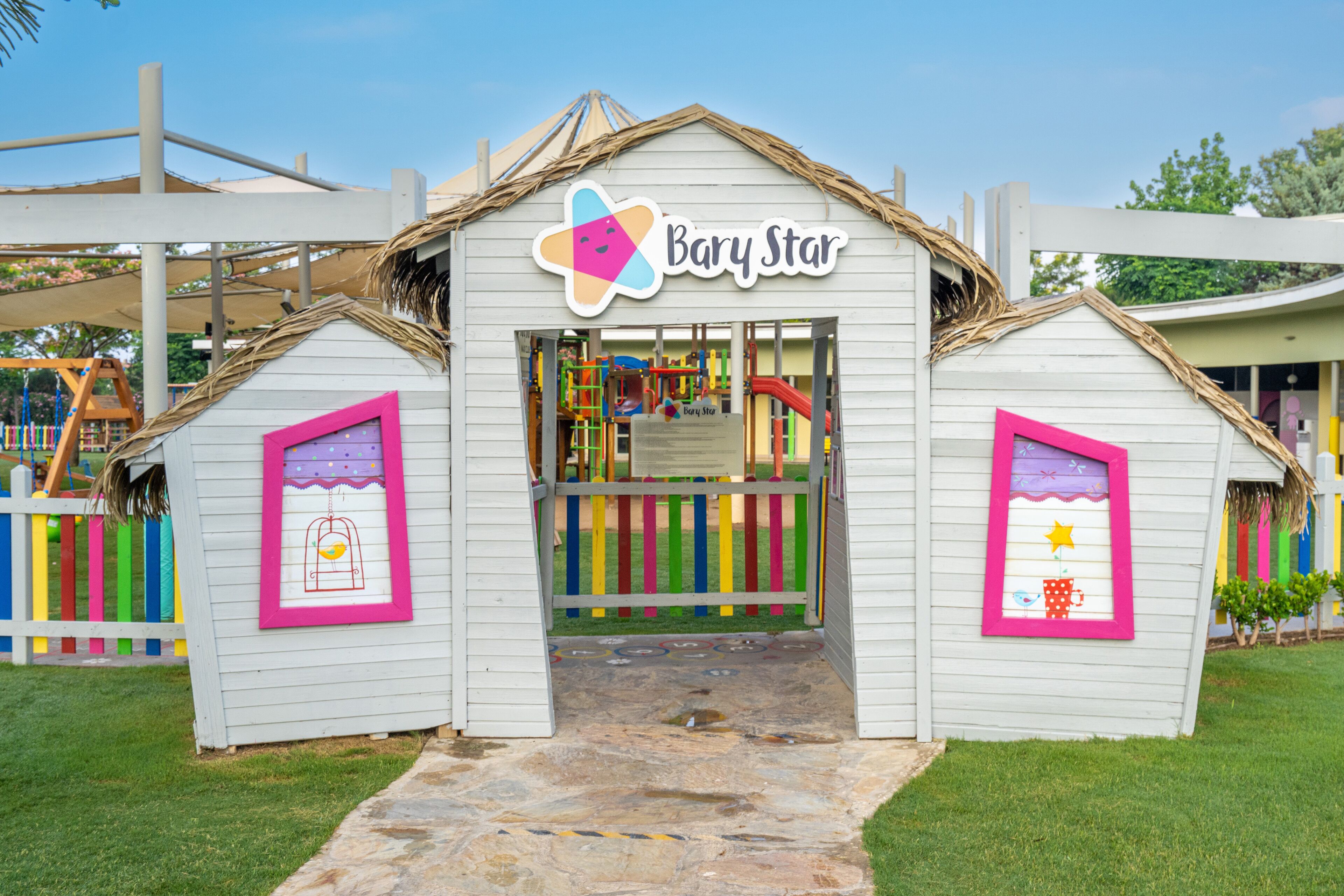 Ein Kinderspielbereich namens 'Bary Star' mit einem Spielhäuscheneingang, bunten Spielgeräten und einer Rasenfläche.