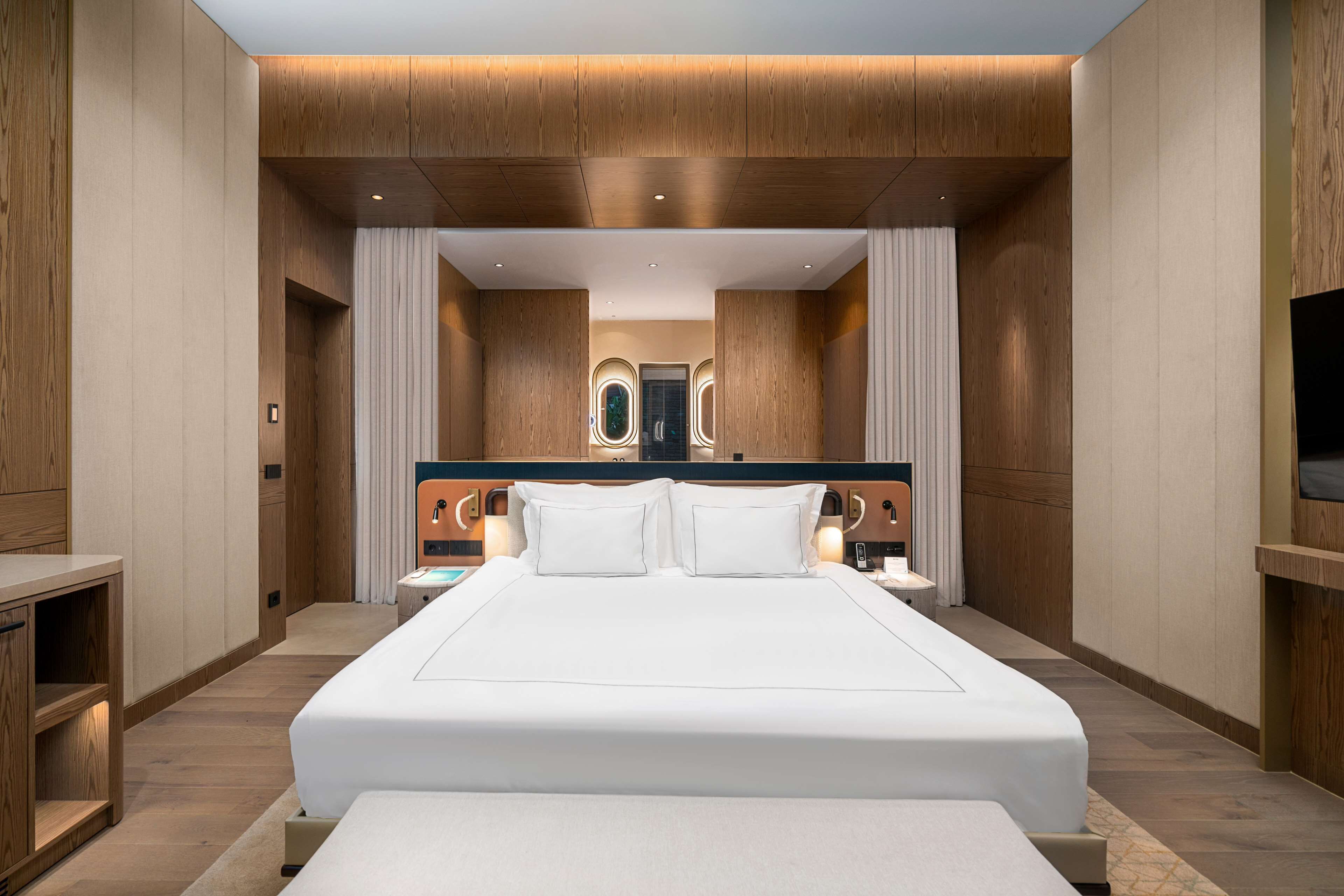 Una habitación de hotel moderna con una cama grande, paneles de madera y un televisor en la pared.