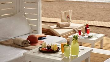 A beachside lounge with a white table, a plate of fruit, and two drinks.