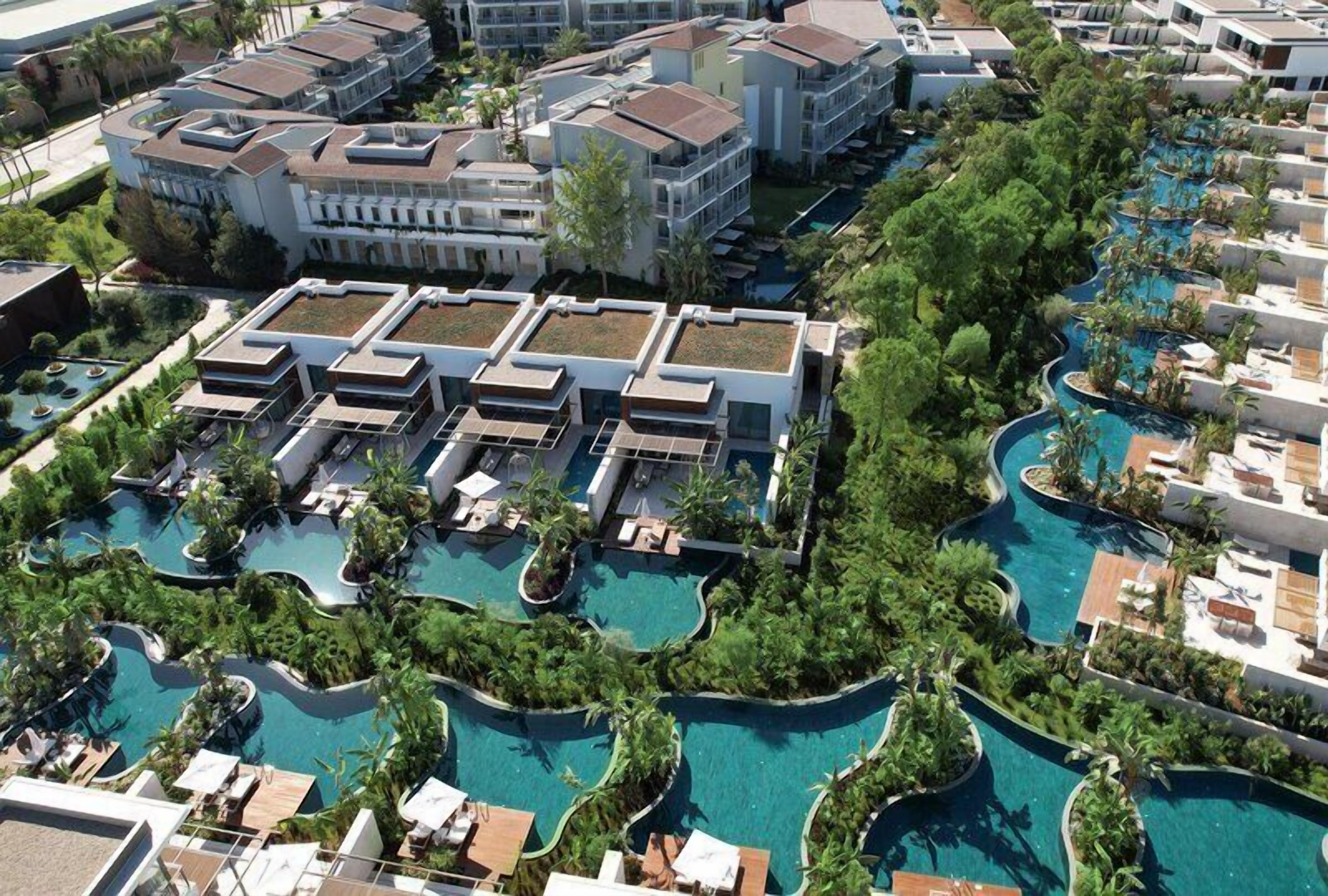 A resort with multiple swimming pools, connected by walkways, and surrounded by lush greenery.