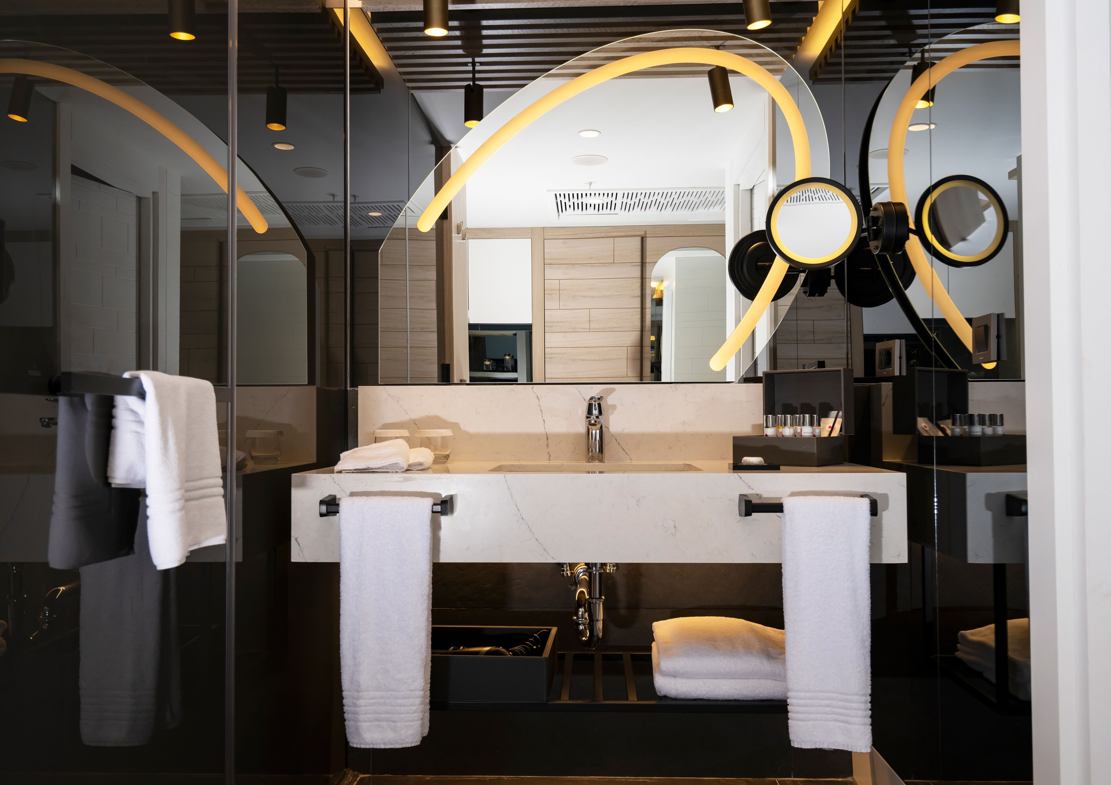 Une salle de bain moderne avec un grand miroir, un lavabo blanc et deux porte-serviettes.