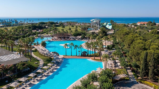 A resort with a large central pool, palm trees, and a view of the ocean.