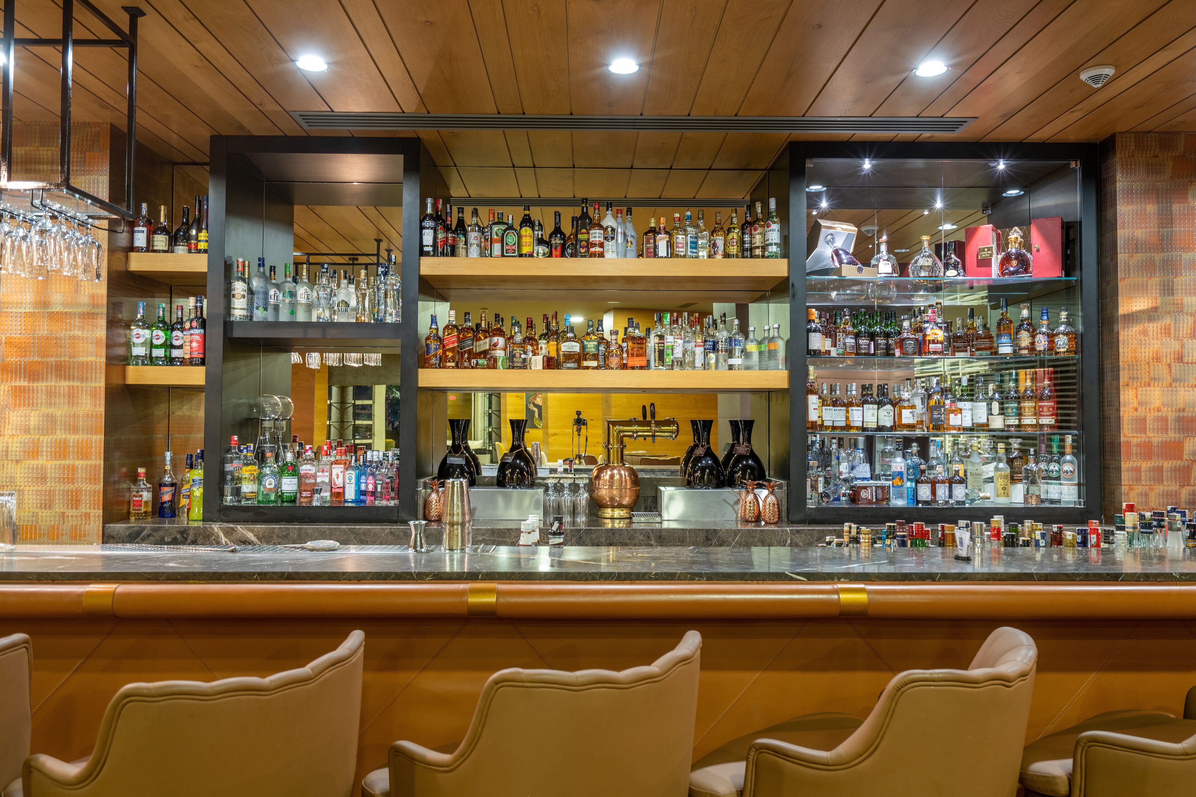 Un espace bar doté de plusieurs étagères remplies de bouteilles d’alcool, d’un comptoir et de tabourets de bar.