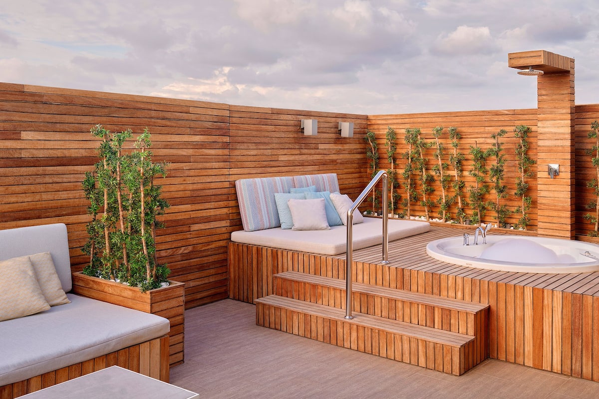 A wooden deck with a hot tub, seating area, and steps leading to a raised platform.