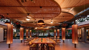 A spacious indoor dining area with a long wooden table and chairs, surrounded by tall, illuminated columns.