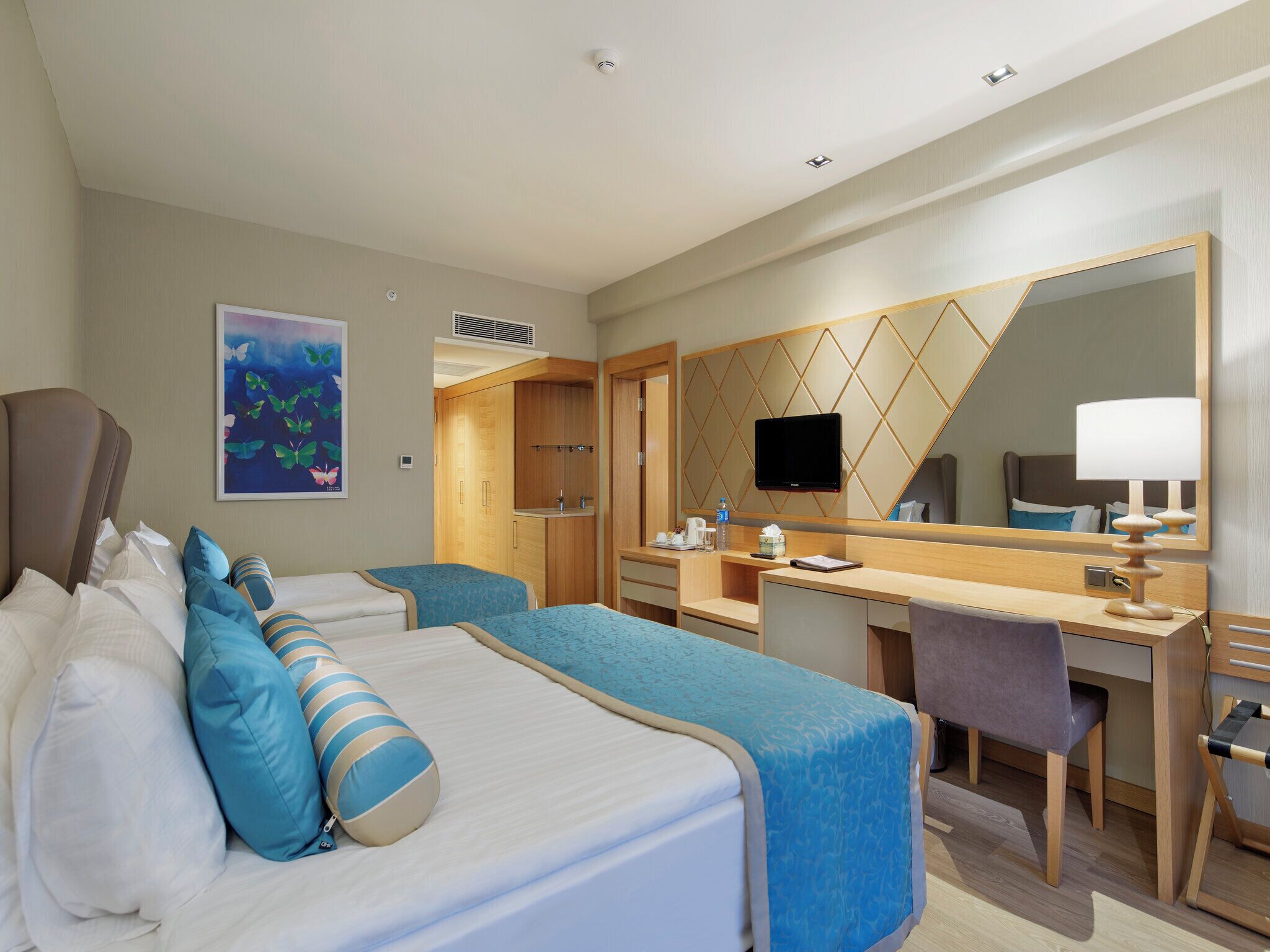 A hotel room with two beds, a desk, a chair, a television, and a mirror.