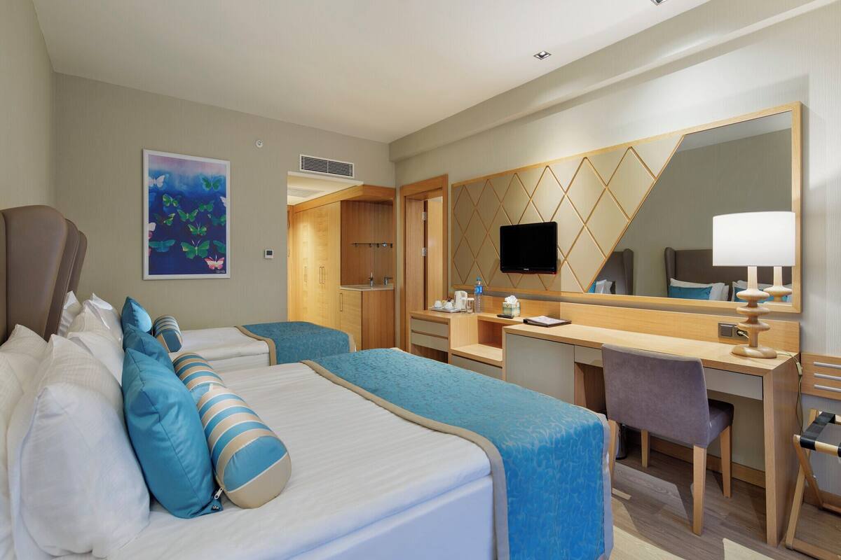 A hotel room with two beds, a desk, a chair, a television, and a mirror.
