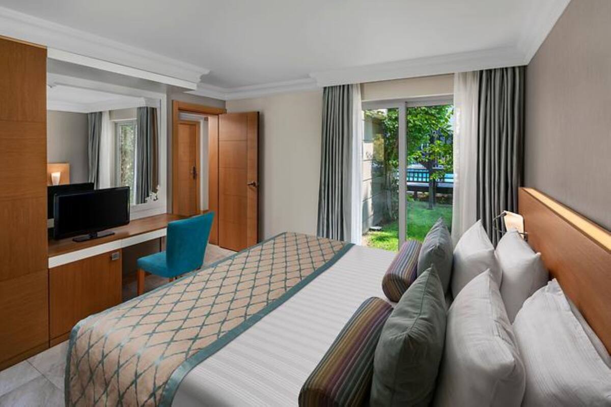 A hotel room with a bed, a desk with a TV, a chair, and a view of the outdoors.