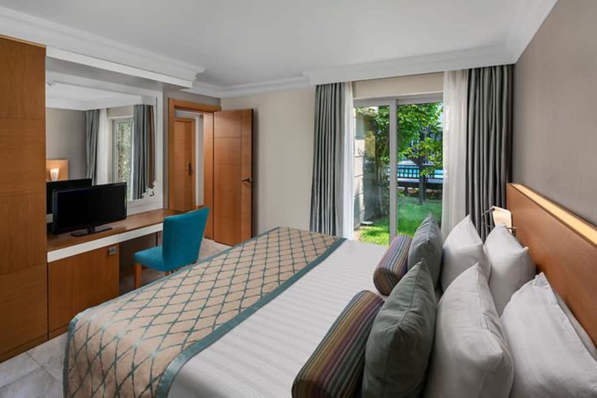 A hotel room with a bed, a desk with a TV, a chair, and a view of the outdoors.