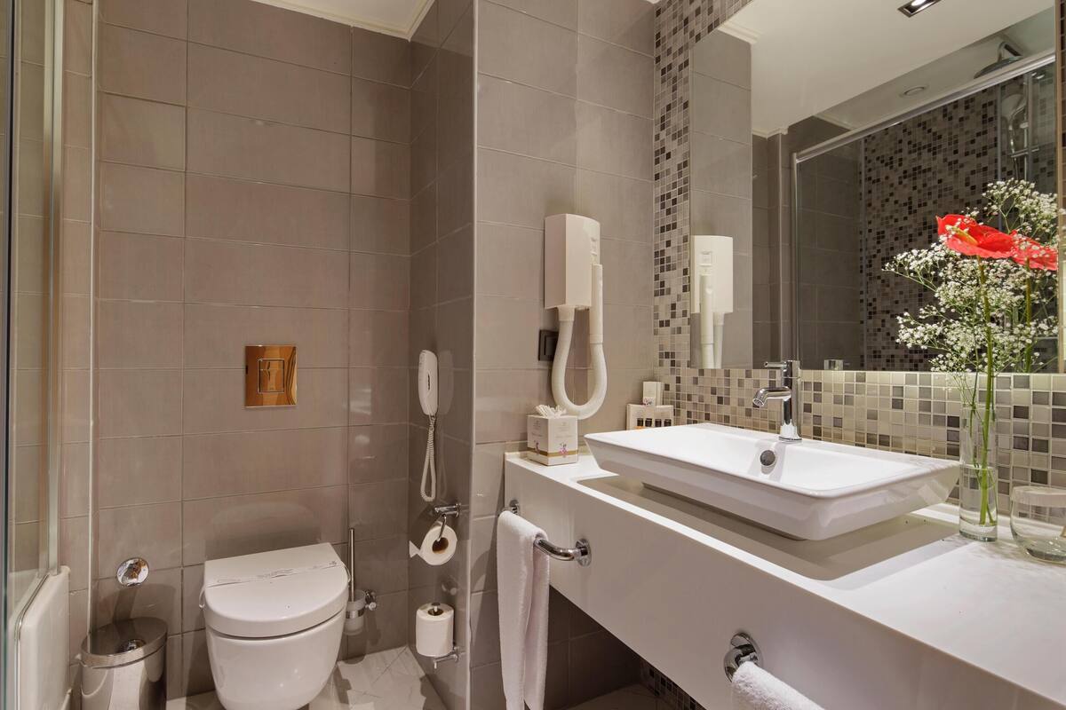 A modern bathroom with a glass shower enclosure, a white toilet, a sink with a mirror, and a decorative vase with flowers.