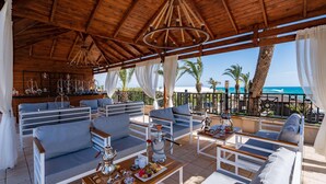 Ein überdachter Außenbereich mit Sofas und Tischen, eine Bar und Meerblick.