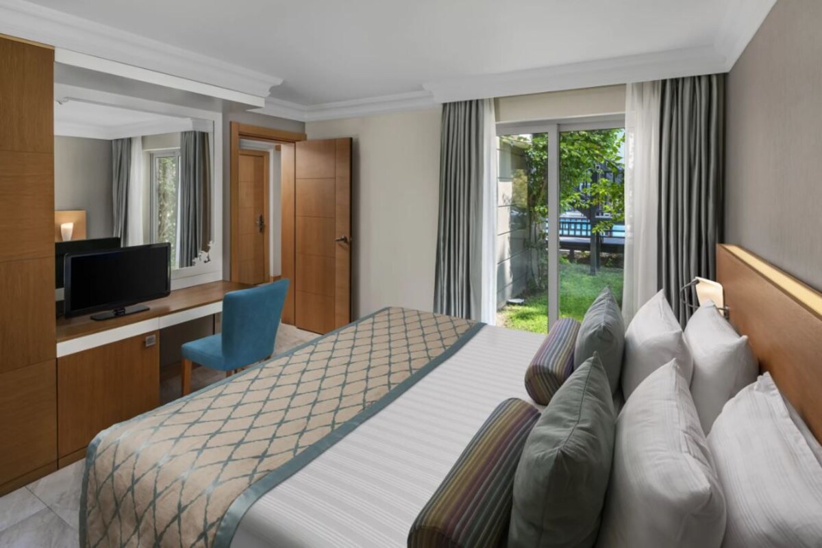 A hotel room with a bed, a desk with a TV, a chair, and a view of a garden through a sliding door.