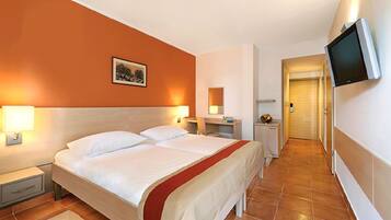 Ein Hotelzimmer mit einem Bett, Nachttischen, einem Fernseher und einem Flur, der zu einer Tür führt.