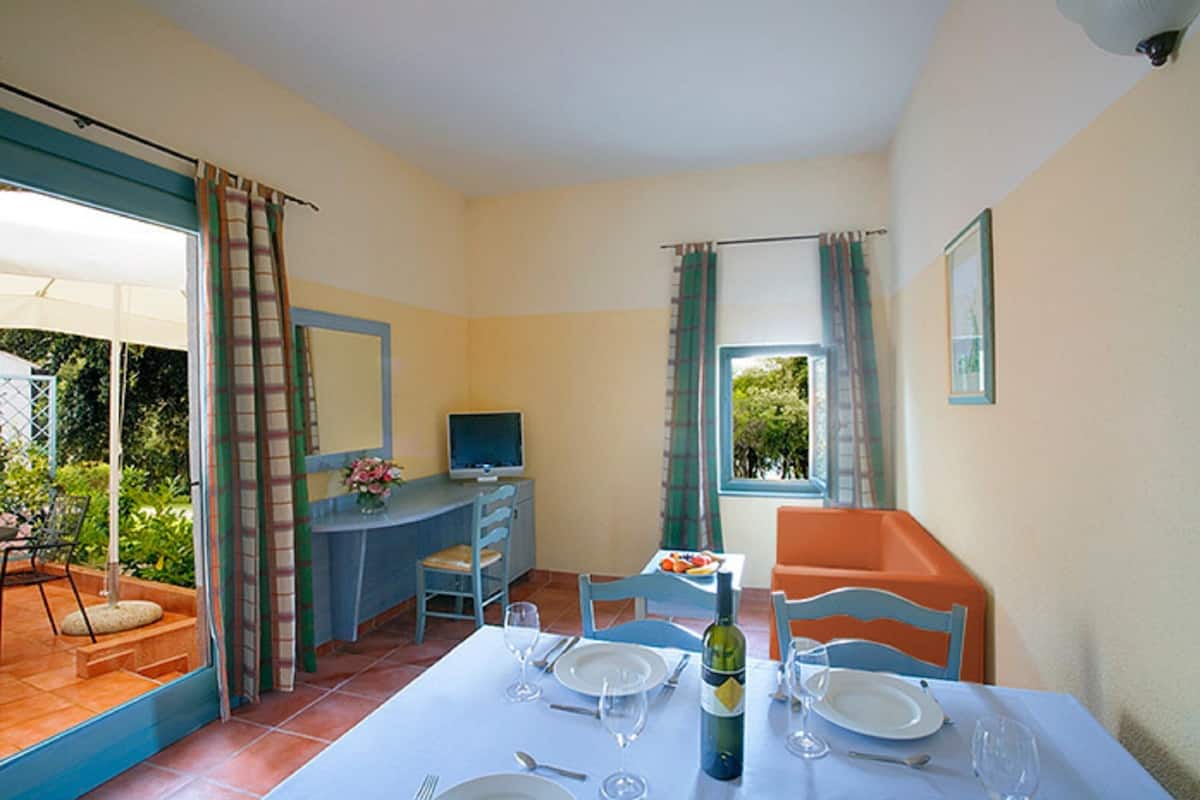 A dining area with a table set for two, a television, and a view of the outdoors.