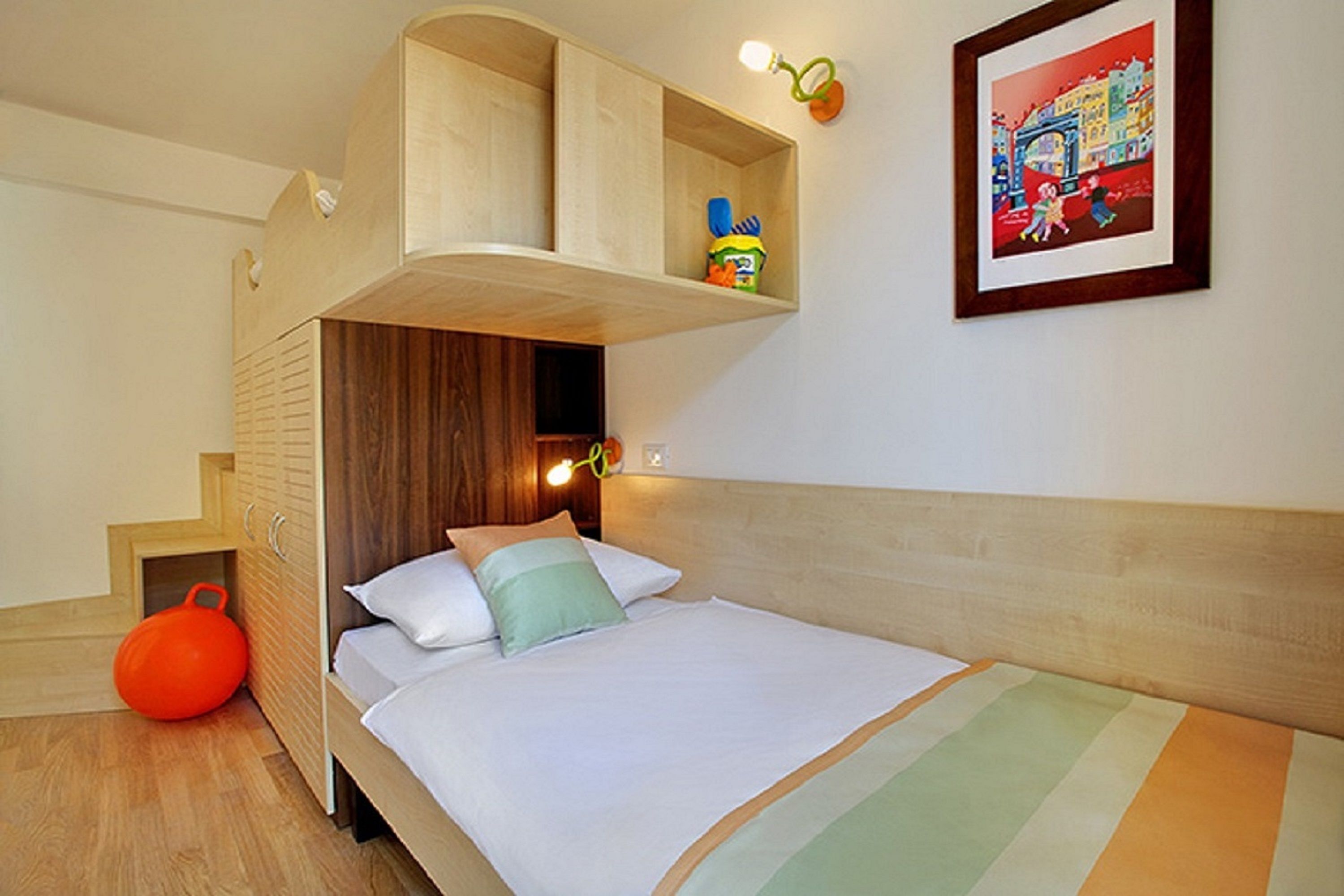 Un dormitorio con una cama litera, un estante pequeño con juguetes, un cuadro en la pared y una colcha a rayas en la cama.
