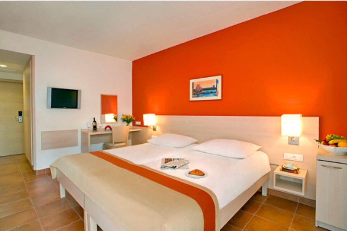 A hotel room with a large bed, two bedside tables, a TV, and a fruit bowl.