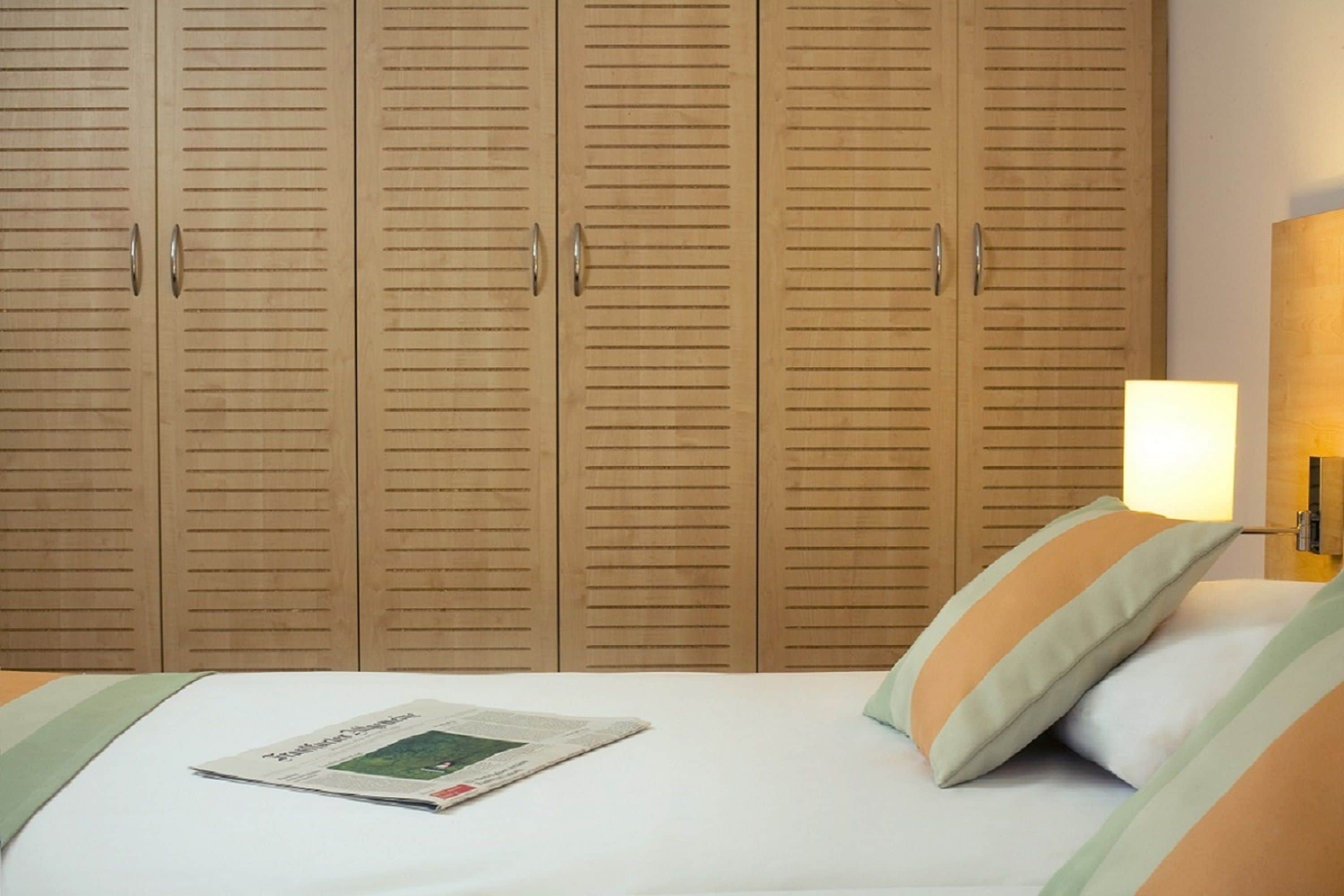 A bedroom with a bed, a newspaper, and wooden wardrobes.