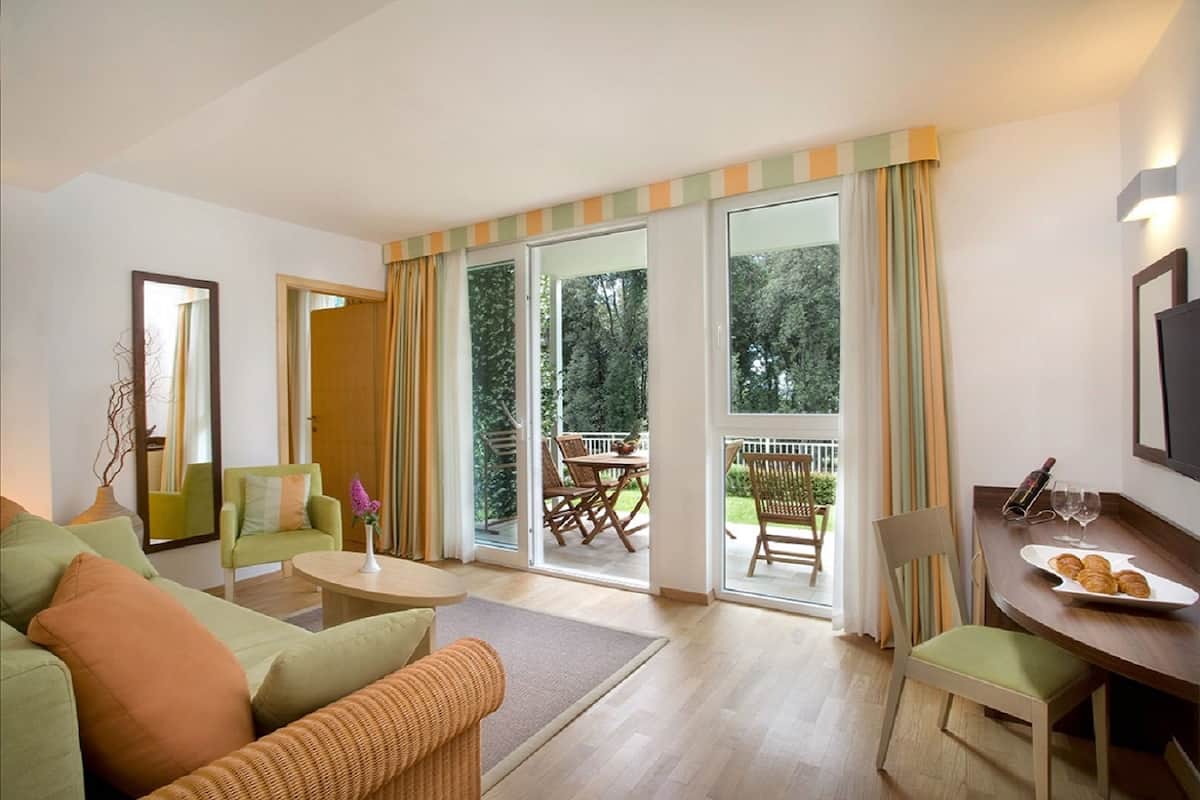 A living room with a sofa, armchair, dining table, and a balcony with outdoor furniture.