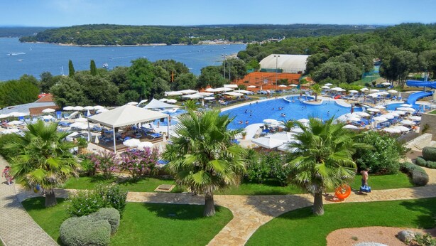 Un resort con una amplia piscina, palmeras y vista al mar.