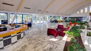 Eine großzügige Lobby mit einer Rezeption, Sitzbereichen und großen Fenstern mit Blick ins Freie.