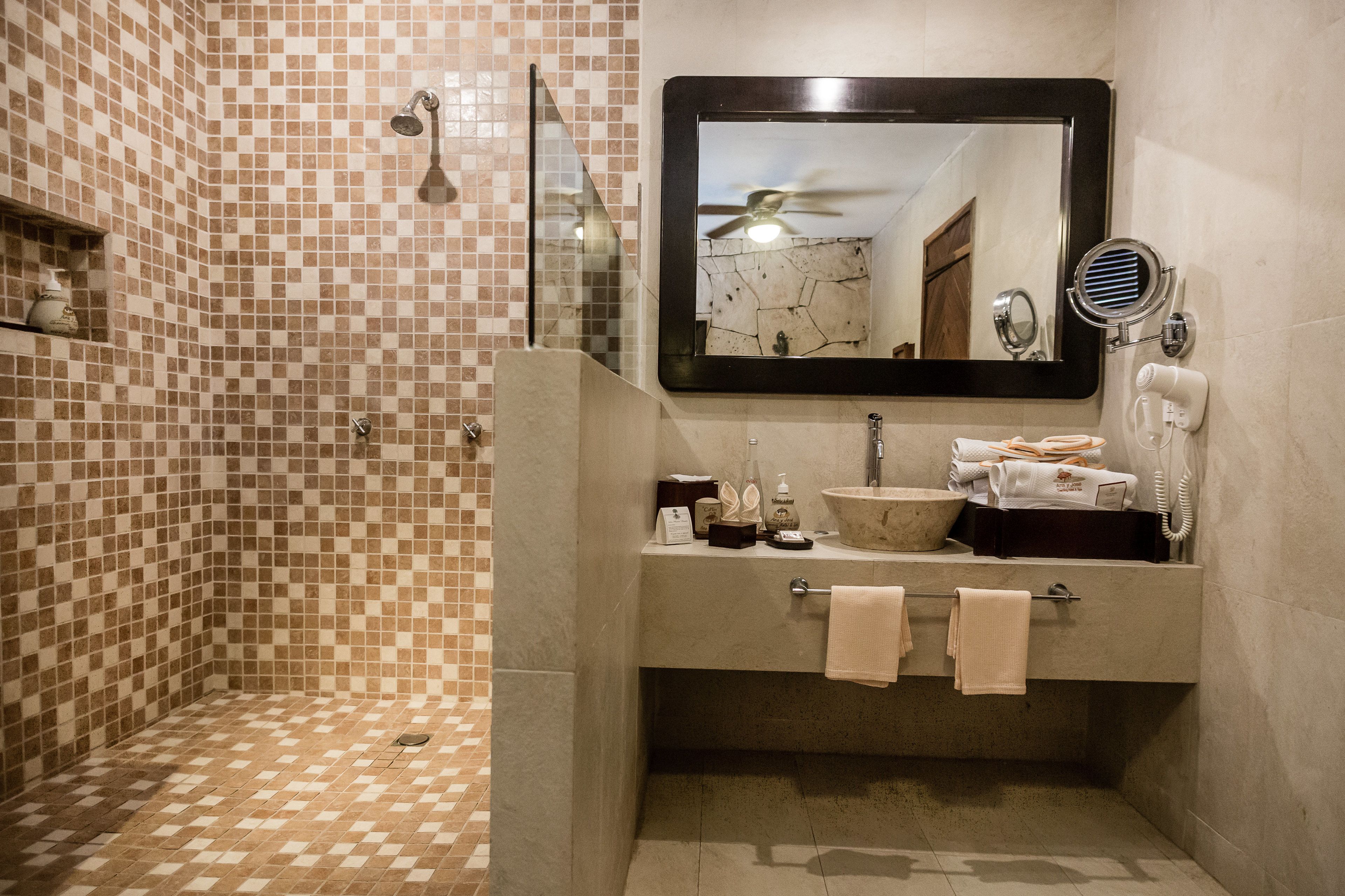 A bathroom with a tiled shower, a sink with a mirror, and a hairdryer on the wall.