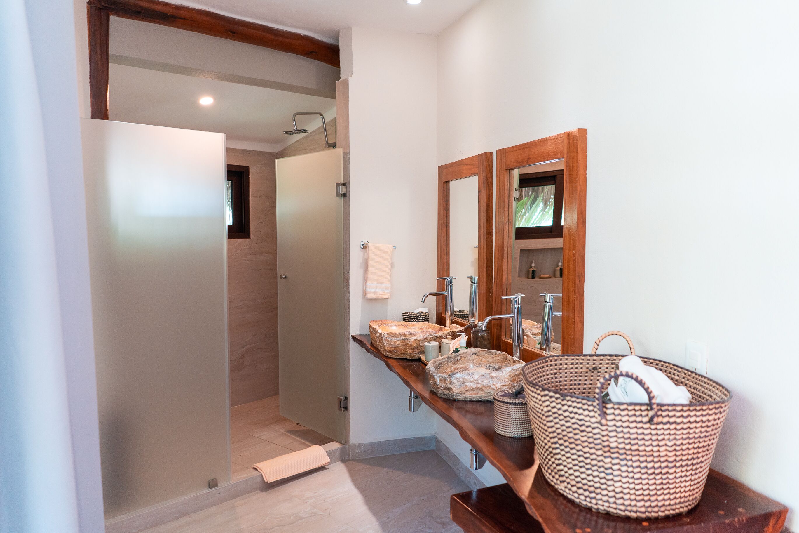 A modern bathroom with a glass shower enclosure, a wooden vanity with a large mirror, and a woven basket on the counter.