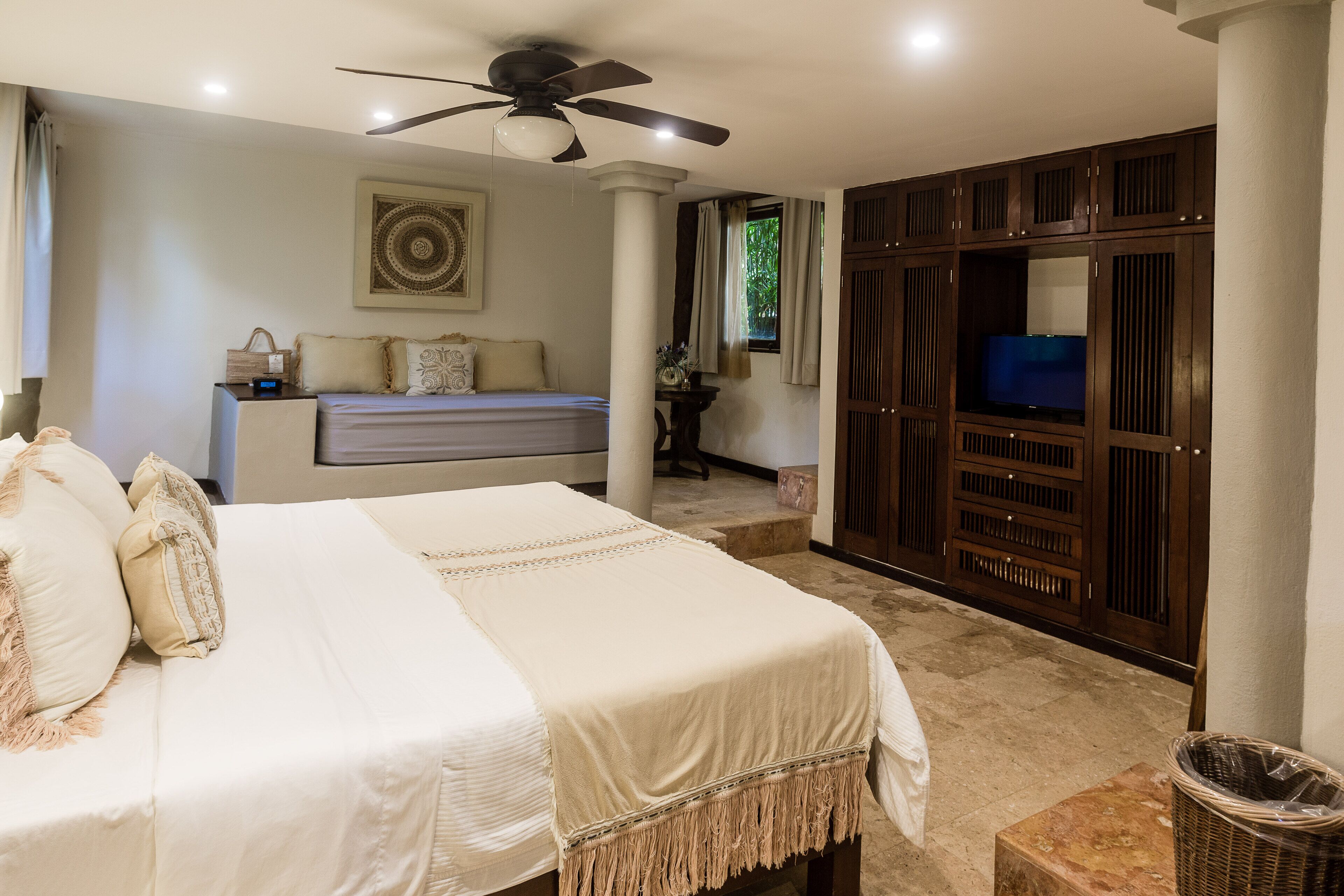 A bedroom with a bed, a ceiling fan, a TV, and a wardrobe.