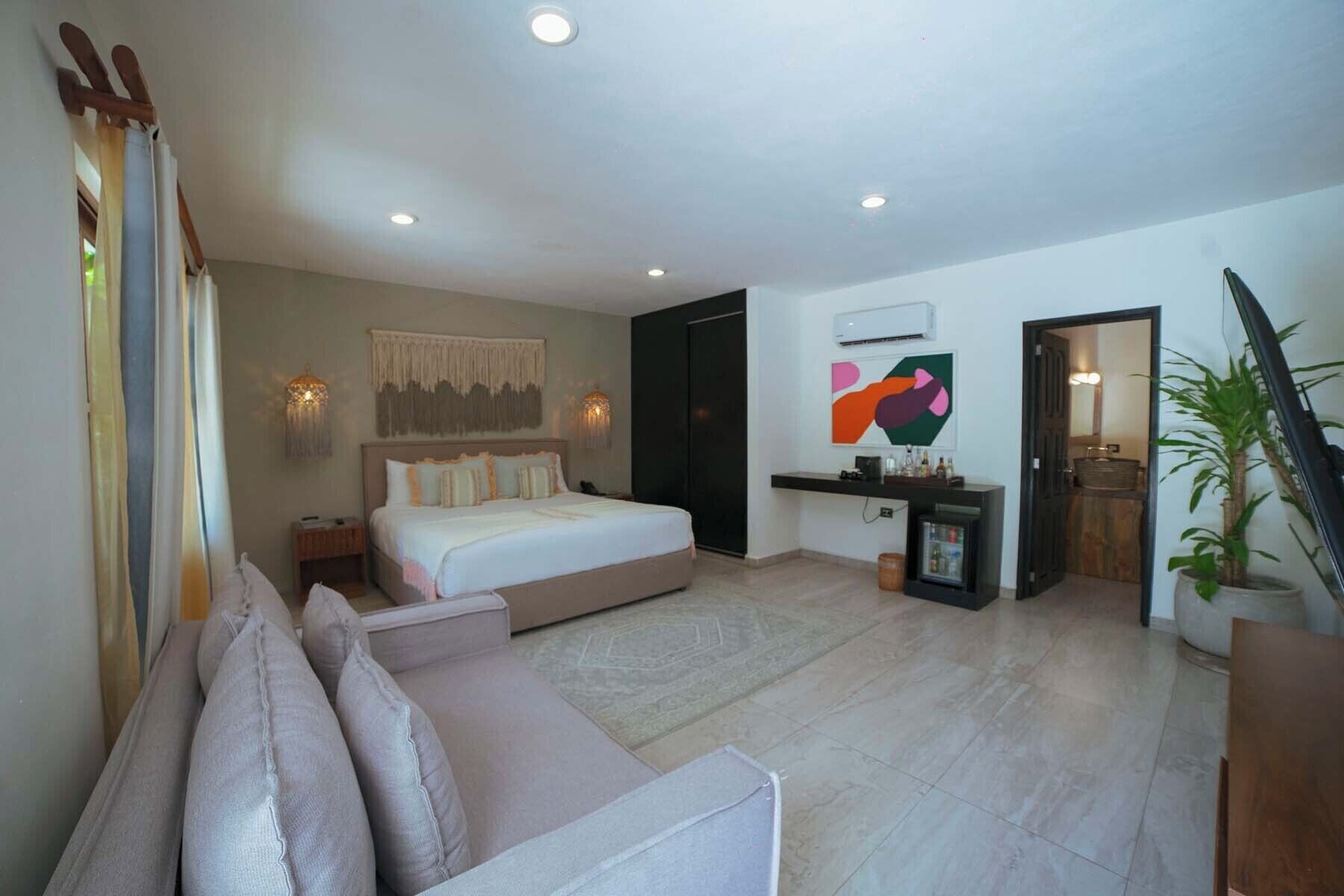 A modern bedroom with a large bed, a sofa, a small table, and a wall-mounted TV.