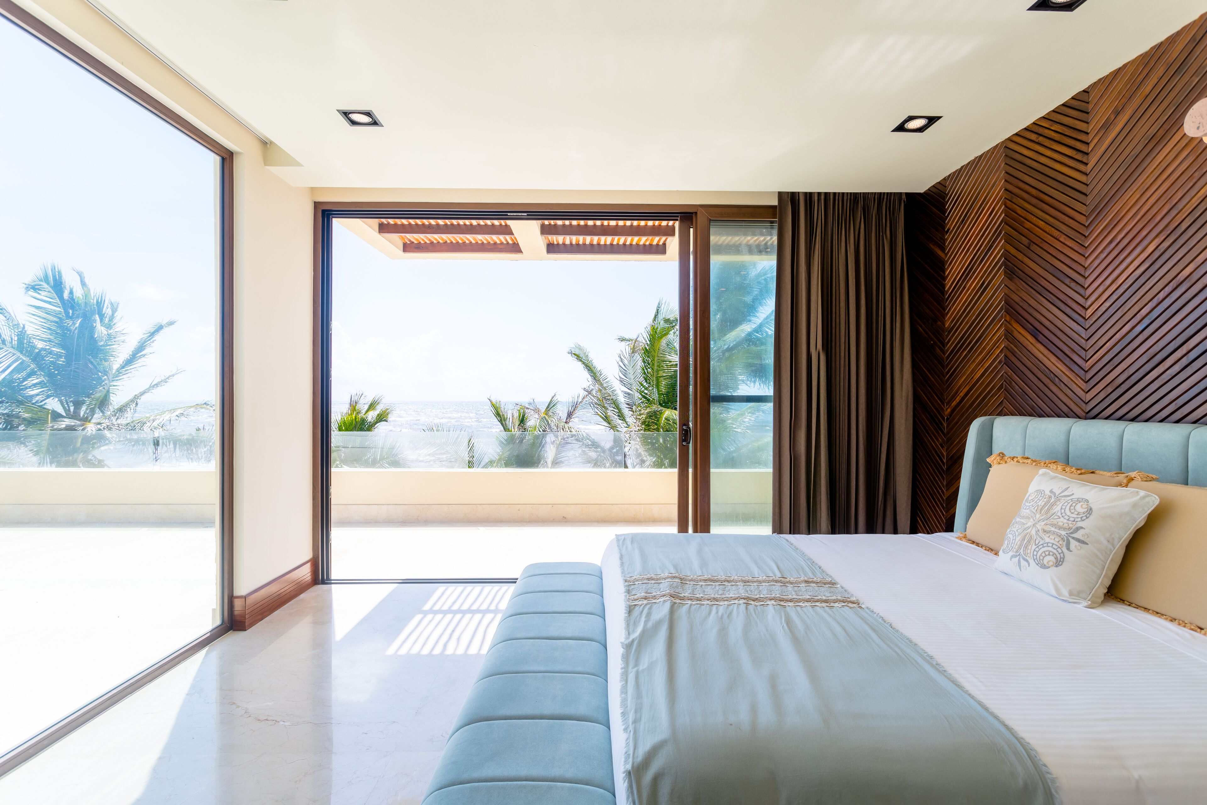 A modern bedroom with a large bed, a view of palm trees, and a balcony.