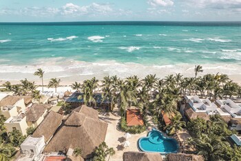 A modern living room with a large flat-screen TV, comfortable seating, a kitchen area, and a glass door leading to an outdoor space. at Ana y Jose Tulum Hotel & Spa