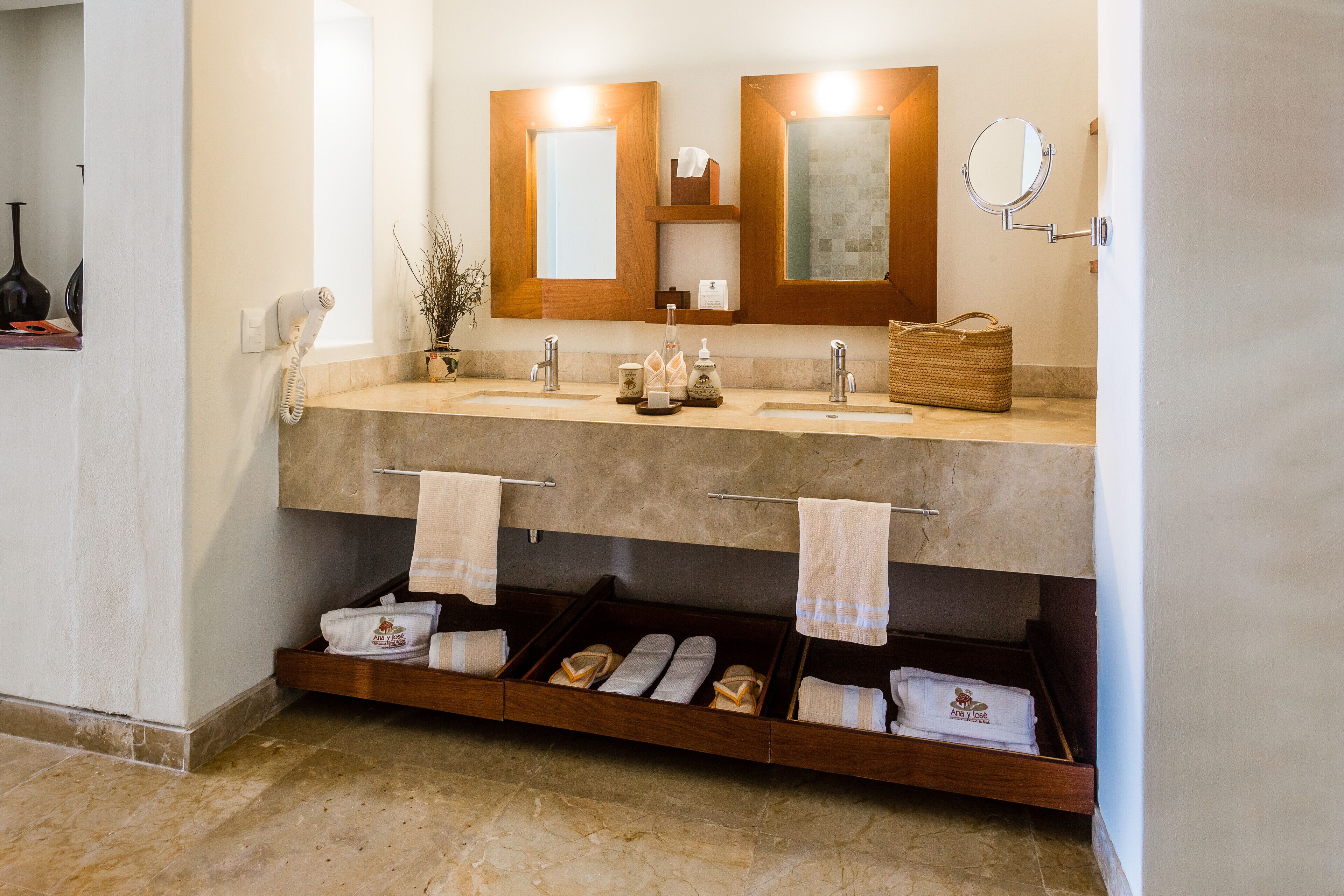 A bathroom with two sinks, a mirror, a towel rack, and a shelf with towels.