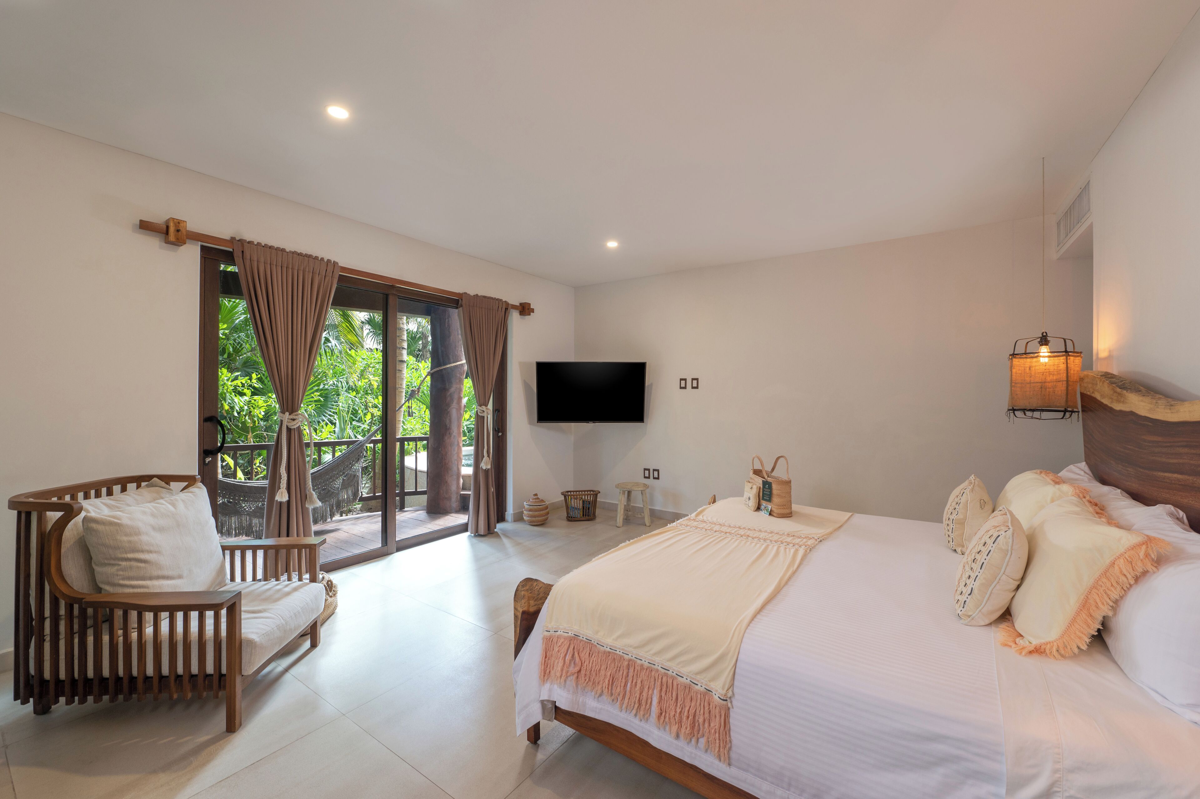 A spacious bedroom with a large bed, a wooden chair, a television, and a view of greenery outside.