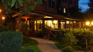 A well-lit outdoor area with a pathway leading to a building with a covered patio and glass doors. - Balletti Park Hotel (Viterbo)