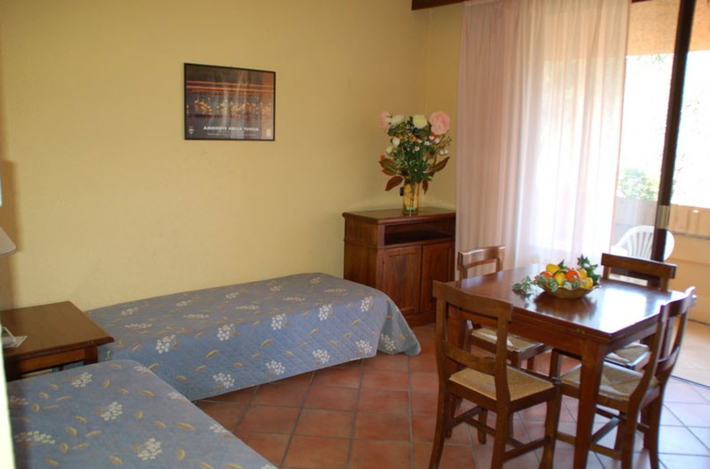 Una habitación pequeña con una cama, un escritorio, una silla y una mesa con un frutero.
