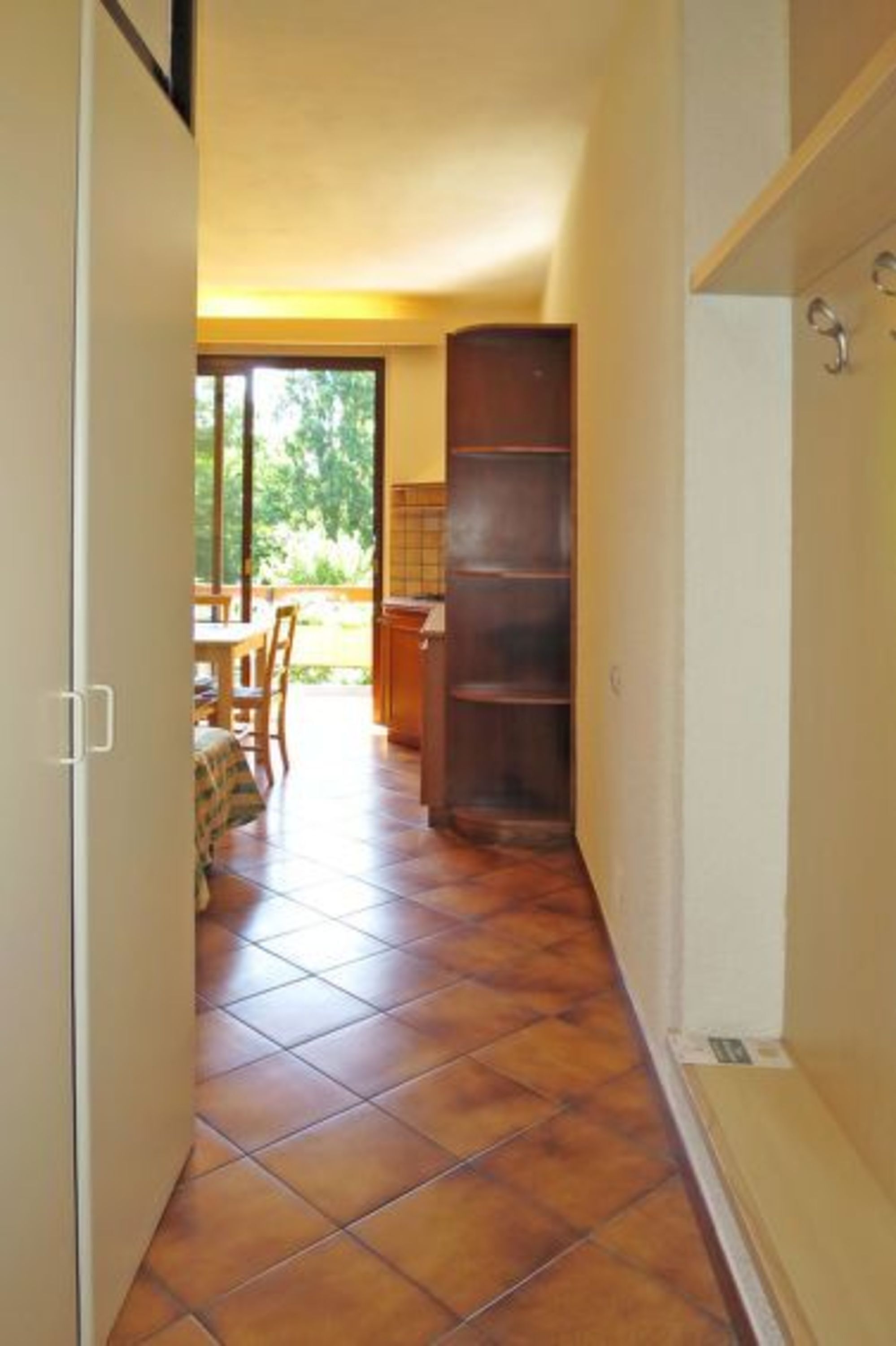 A narrow hallway with tiled flooring leading to a dining area with a table and chairs.