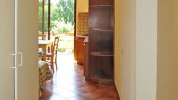 A narrow hallway with tiled flooring leading to a dining area with a table and chairs.