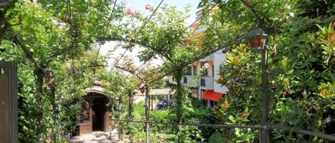 A garden pathway with a pergola covered in climbing plants and flowers, leading to a building entrance.