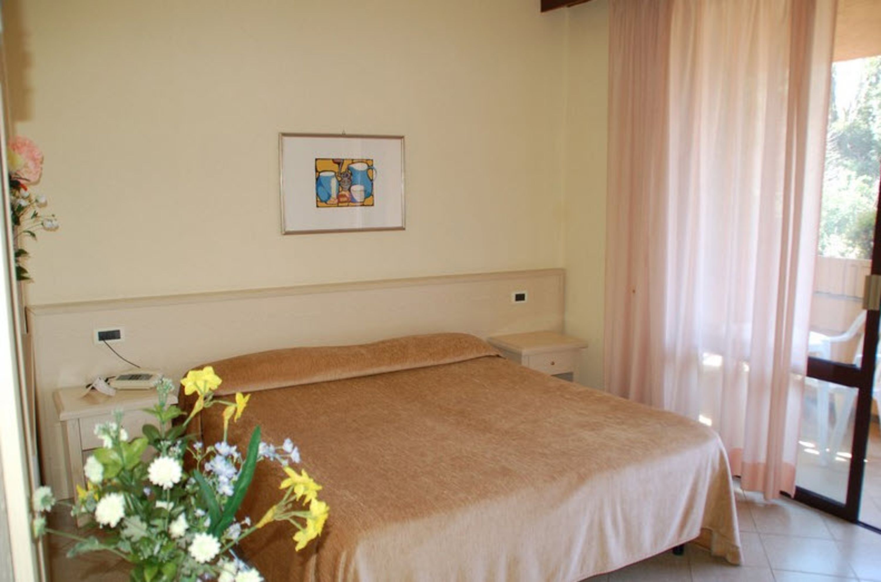 A bedroom with a bed, a bedside table, a wall-mounted telephone, and a framed picture.