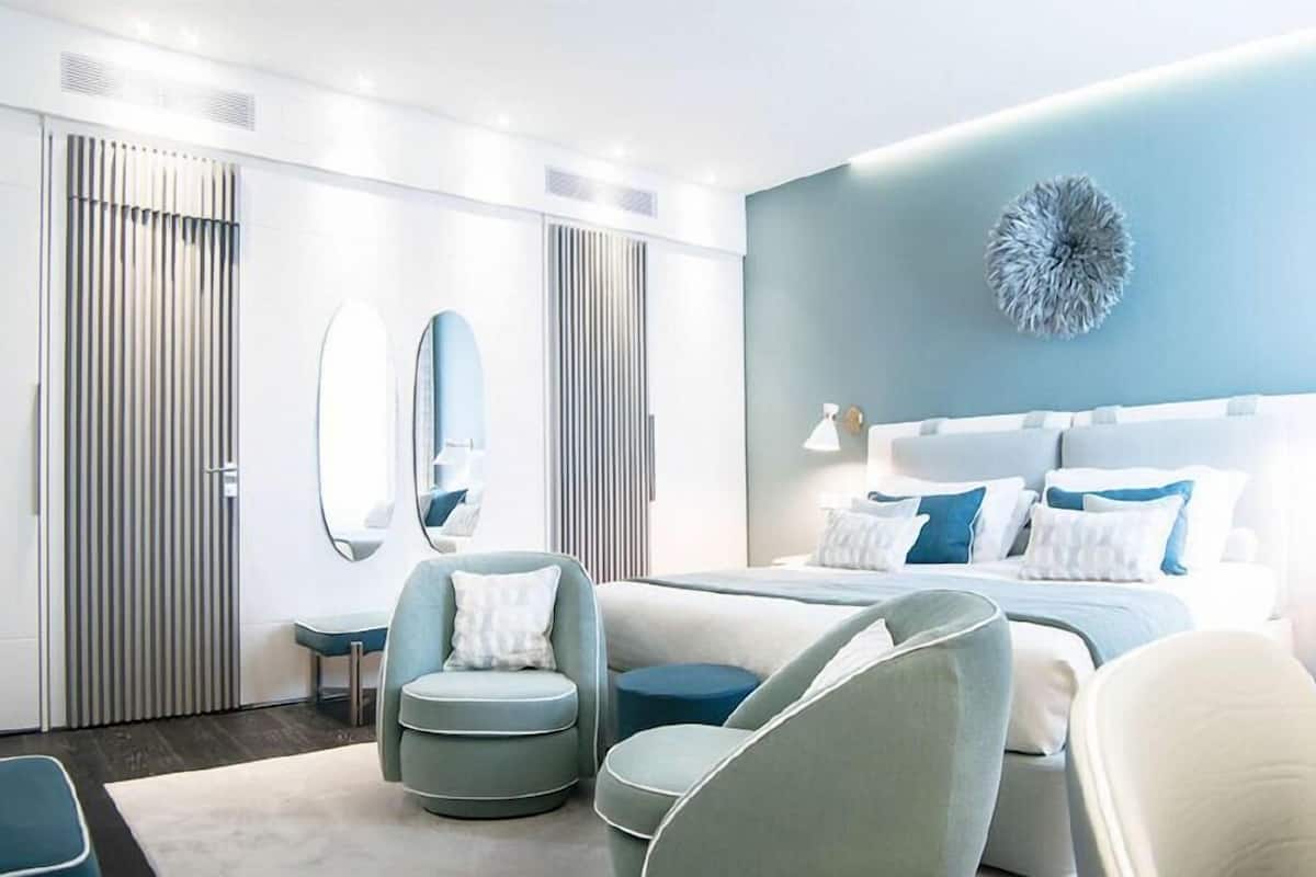 A modern bedroom with a bed, two chairs, a round table, and a large mirror.
