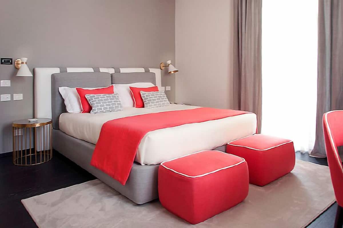 A modern bedroom with a grey headboard, red accents, and a bedside table with a lamp.
